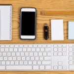 Organized at work: keyboard, phone, thumb drive, note pads, pencils laid out symmetrically on desk