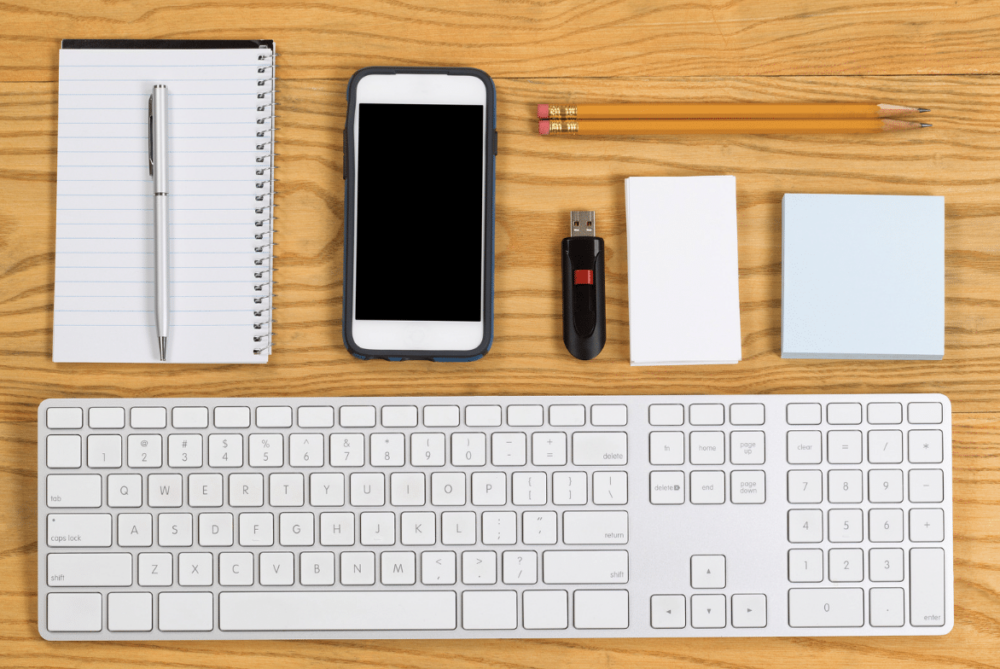 Organized at work: keyboard, phone, thumb drive, note pads, pencils laid out symmetrically on desk