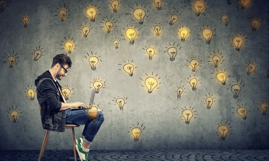 man entrepreneur sitting in chair with laptop, surrounded by drawings of lightbulbs