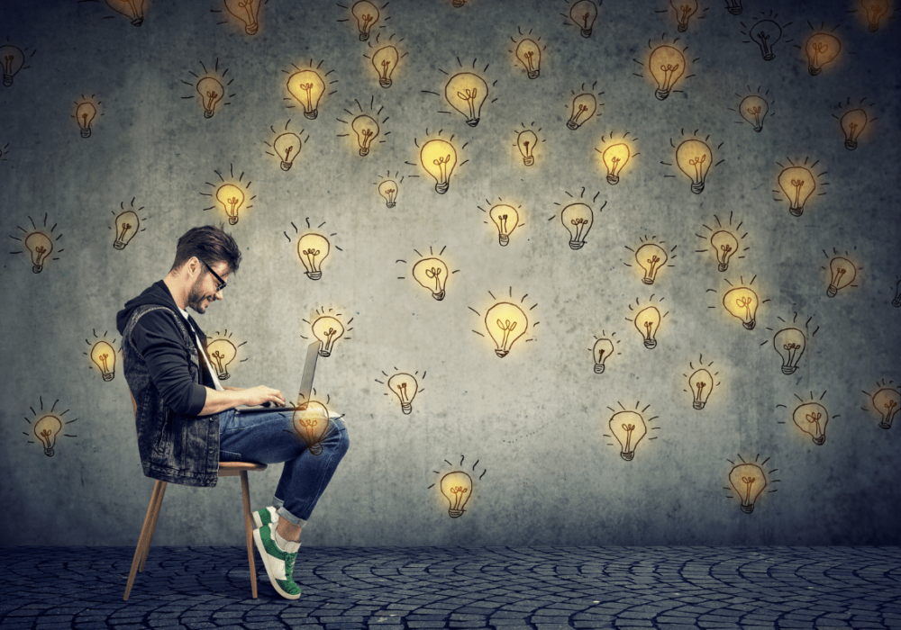 man entrepreneur sitting in chair with laptop, surrounded by drawings of lightbulbs
