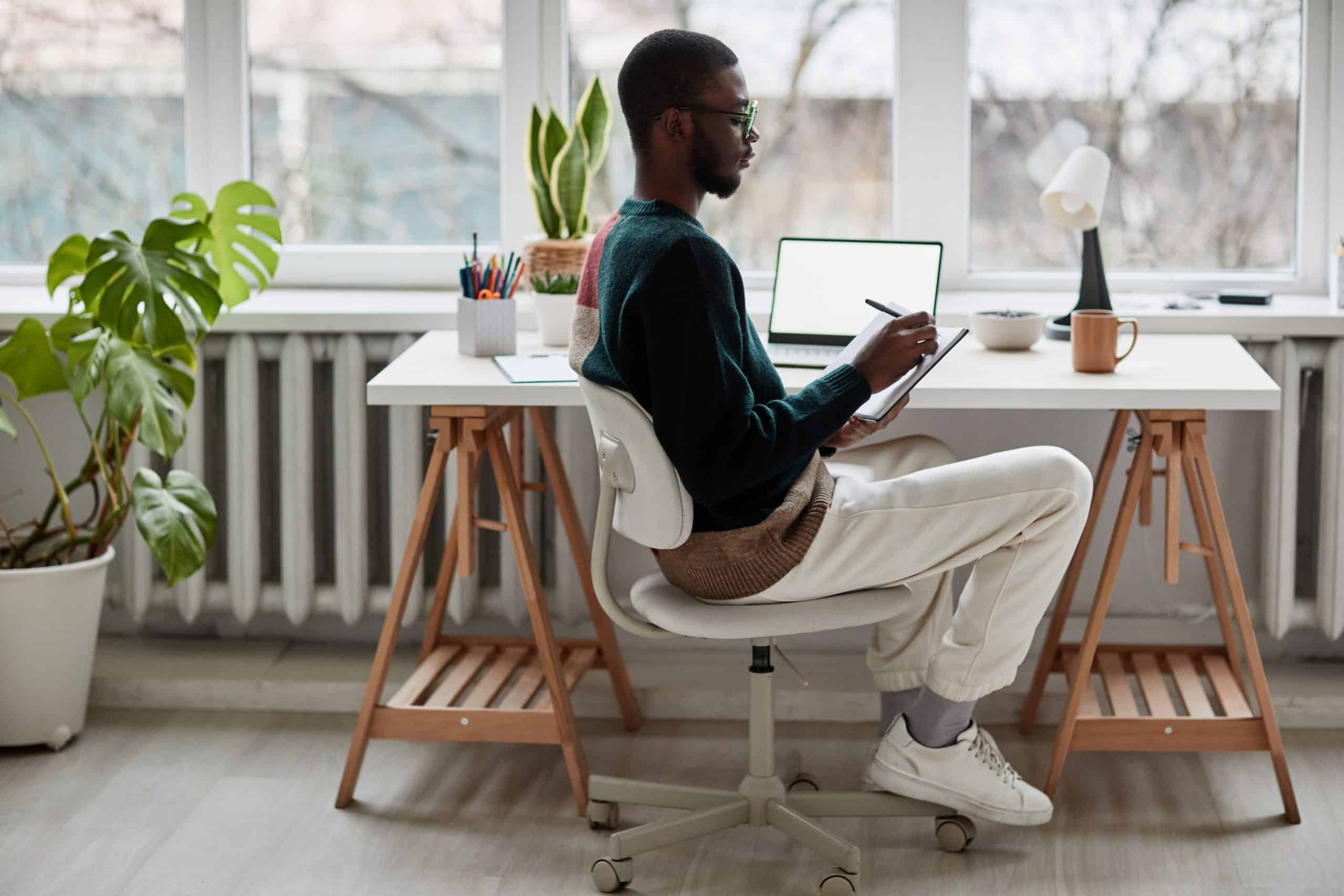 Full length side view portrait of young African-American man wearing glasses while working from home, copy space