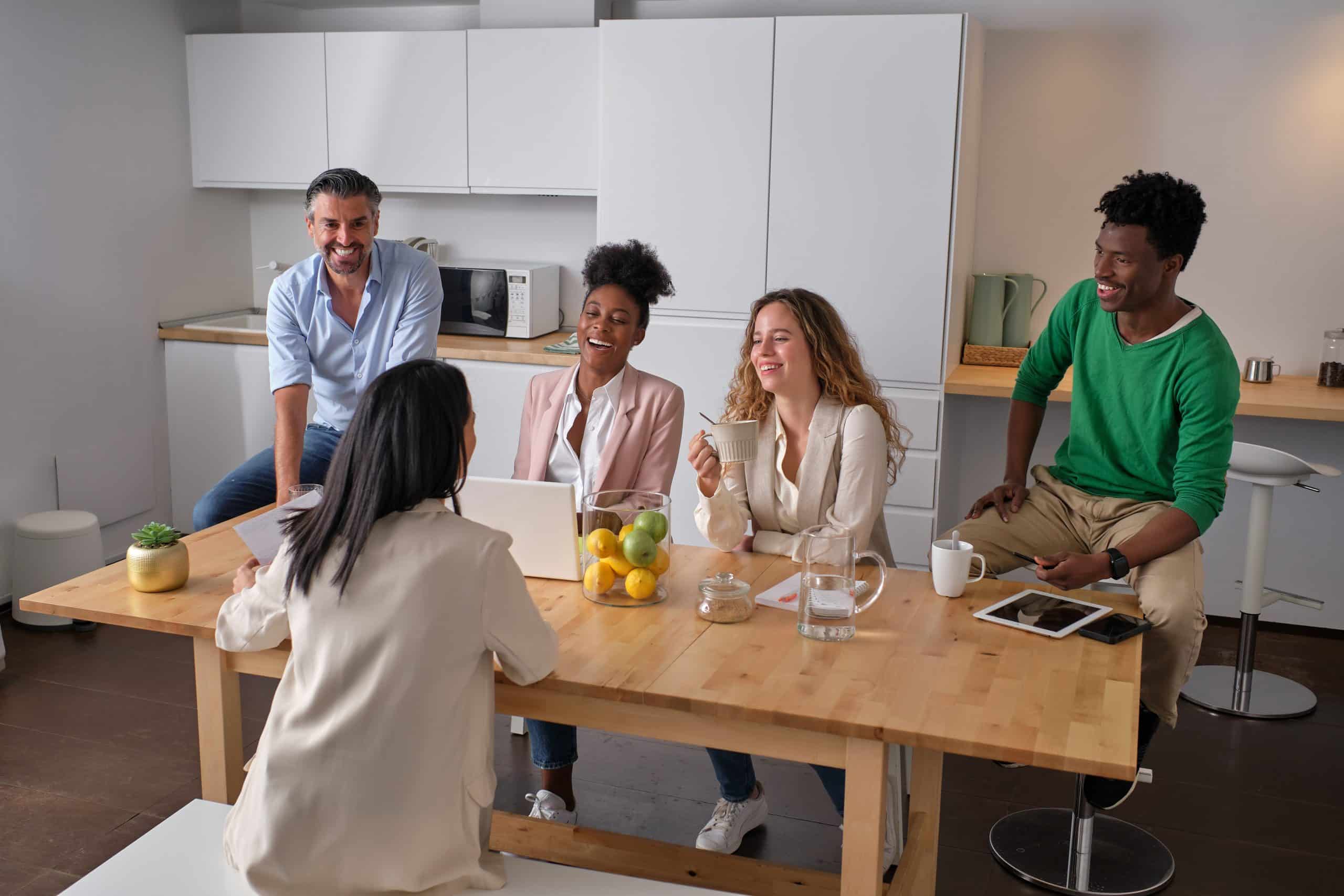 High angle of group of diverse coworkers gathering at table in kitchen and discussing project during break
