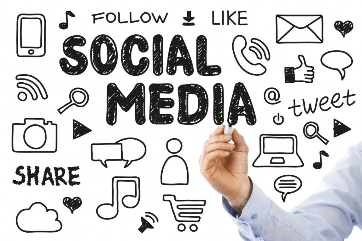 Person holding black marker and writing "Social Media" on board with social media icons.