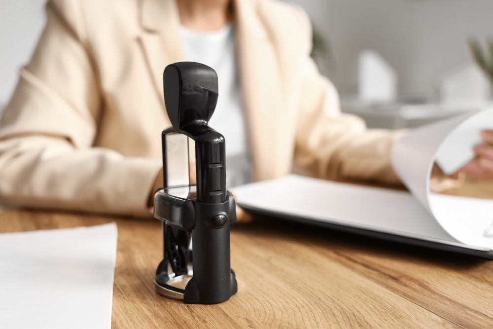 Notary stamp on a desk in front of a woman who is looking at papers.