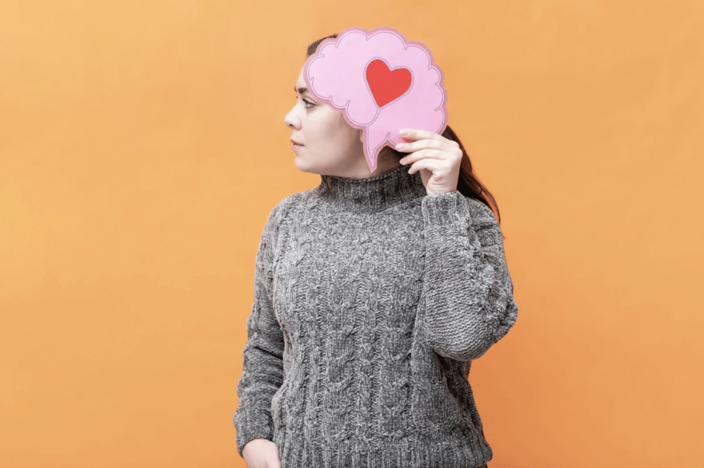 Woman holding a drawing of a brain that has a red heart shape in the middle of it.