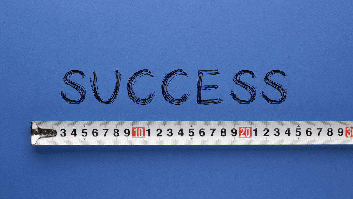 A white measuring tape is beneath the word "success," which is written and displayed on a dark blue background.
