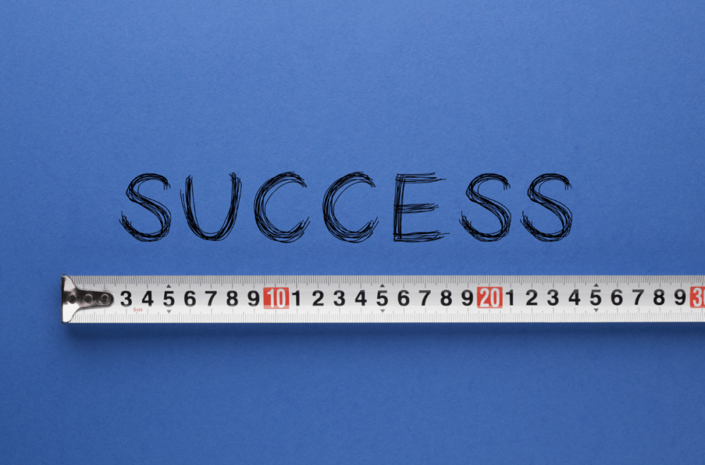 A white measuring tape is beneath the word "success," which is written and displayed on a dark blue background.