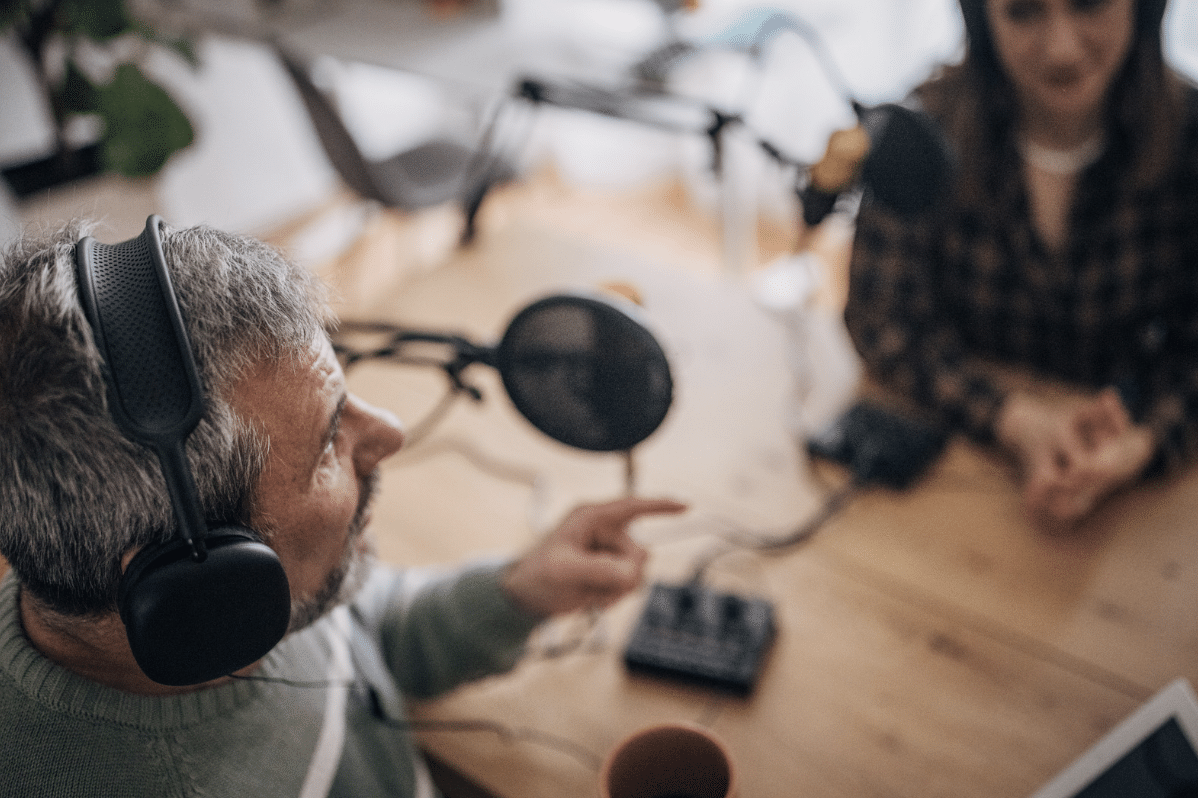 A man wearing headphones is talking on a podcast with a woman sitting across from him.
