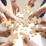 Team members reach their hands out to put puzzle pieces together in a circle.