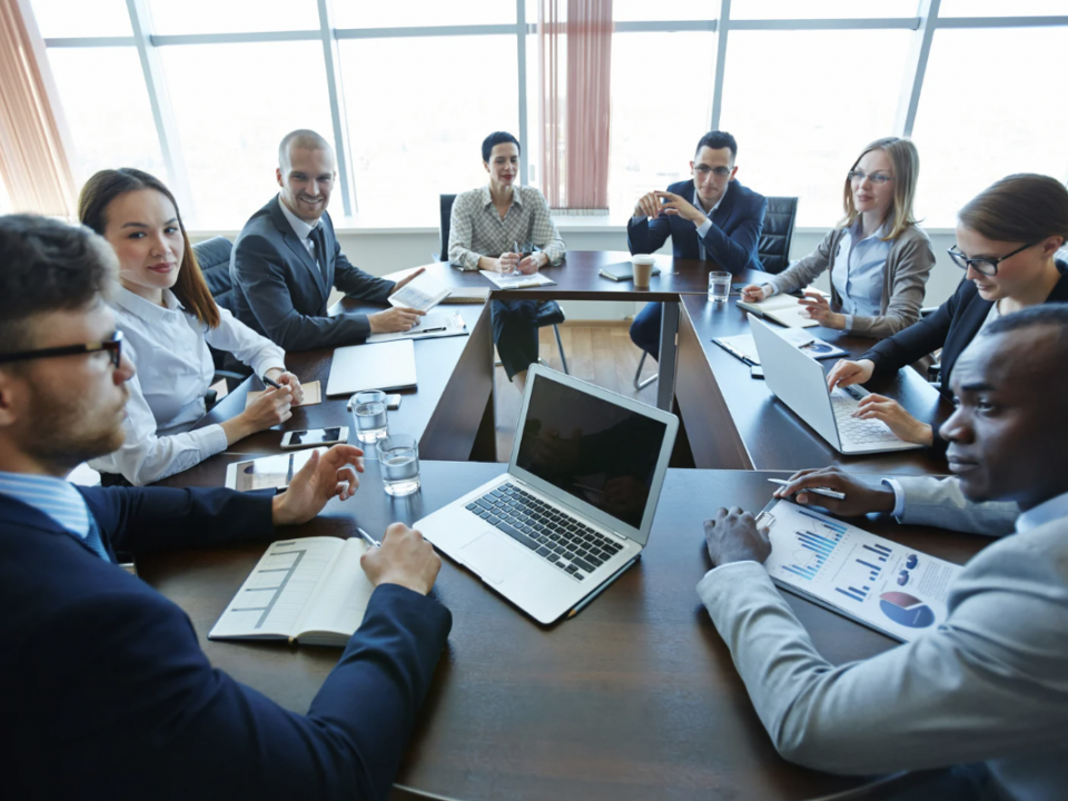 business meeting: diverse group of people sitting around a conference table with laptops and notepads