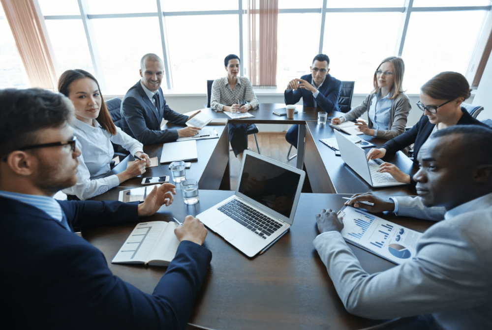 business meeting: diverse group of people sitting around a conference table with laptops and notepads ‣ NuvoDesk Coworking business meeting: diverse group of people sitting around a conference table with laptops and notepads