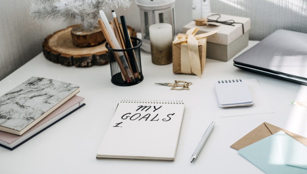 "My Goals" written on a tablet sitting on a desk surrounded by winter decor and office supplies