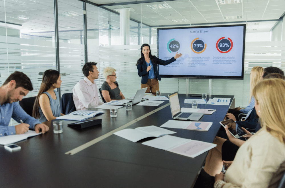 woman giving a presentation in a conference room to colleagues ‣ NuvoDesk Coworking woman giving a presentation in a conference room to colleagues
