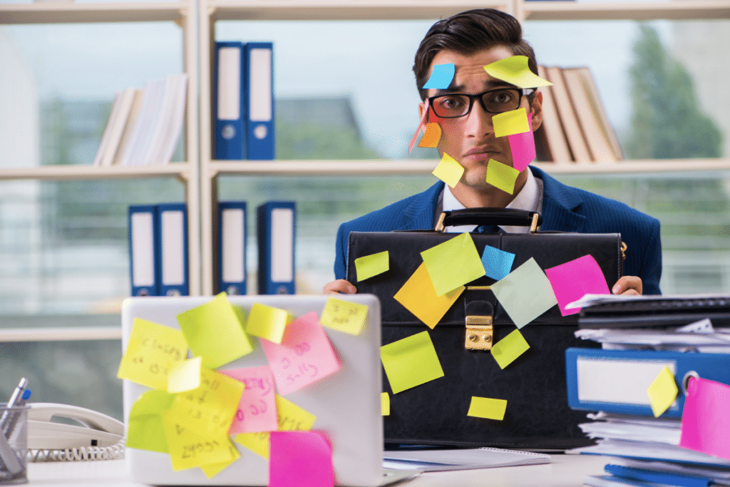 business man at desk covered in sticky notes: This Is The Number One Reason You’re Not Being Productive