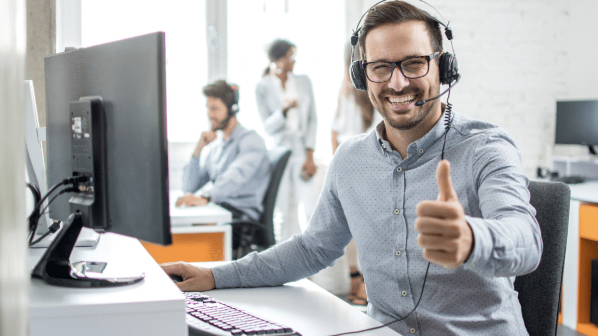 Male virtual assistant with headphones in front of computer giving thumbs up