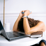 Woman lays head on desk in front of laptop