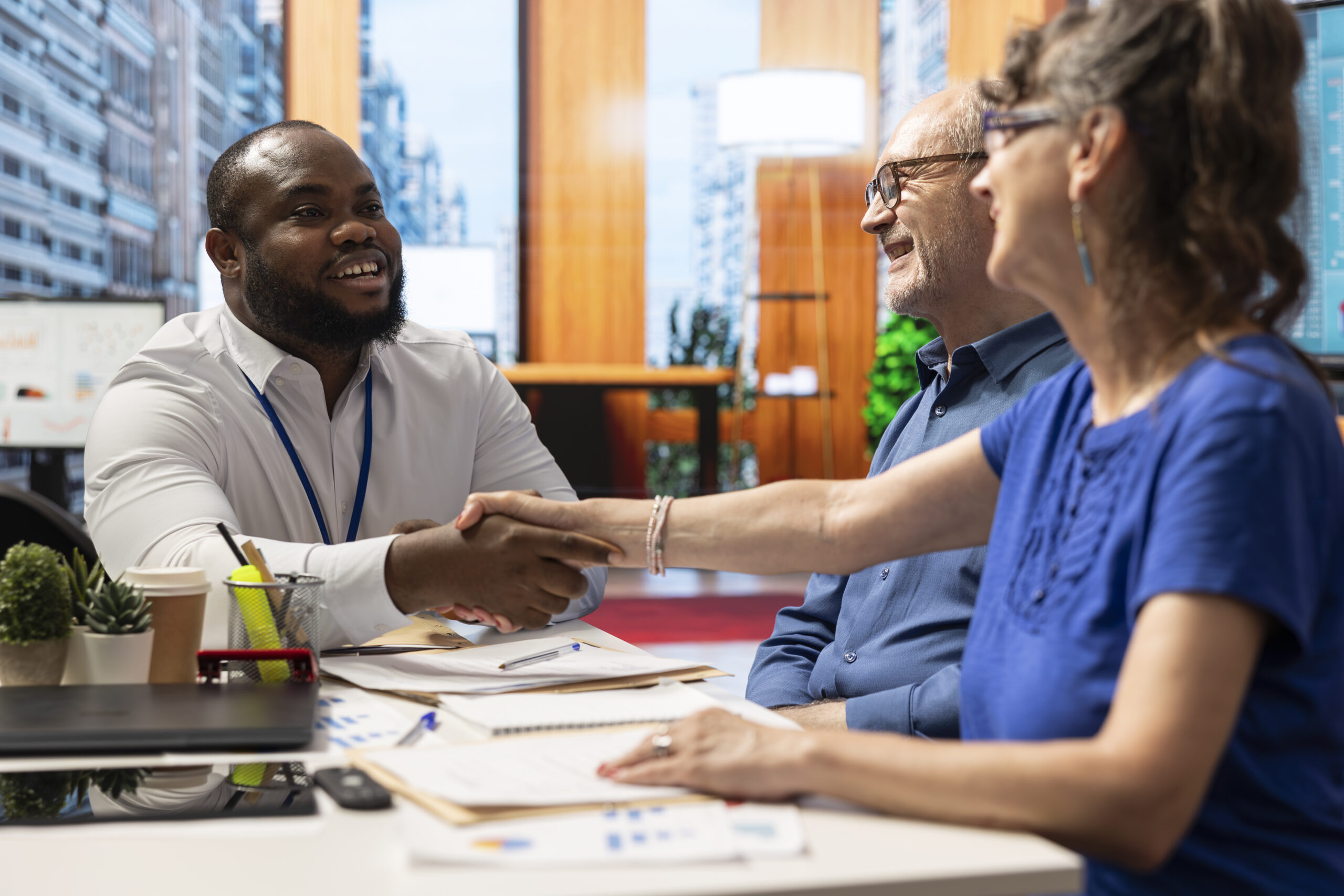 Financial expert sharing a handshake with old woman client during a counseling meeting in modern office. Adviser guiding senior people to choose a retirement plan with life insurance.