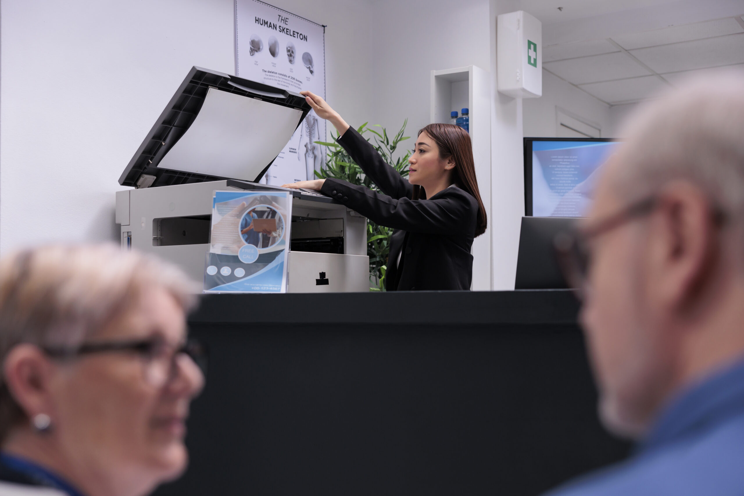 Secretary using copy printer at reception counter to make report papers before checkup consultations. Woman receptionist working on healthcare appointments with forms at registration desk.