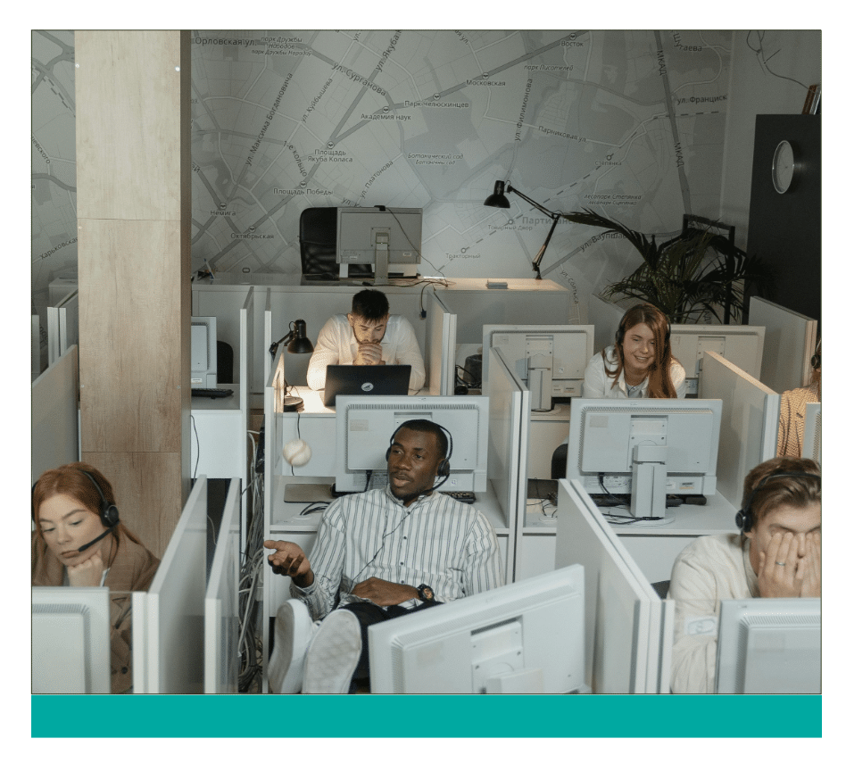 87 ‣ NuvoDesk Coworking Busy call center with employees working in cubicles; some are on headsets, one person is tossing a stress ball, and others appear tired or stressed, reflecting varied workplace moods.