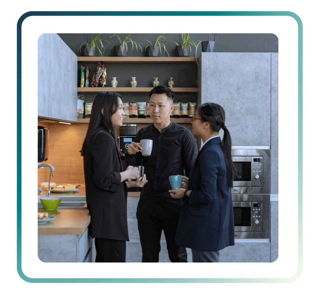 120 ‣ NuvoDesk Coworking Three colleagues chatting and holding coffee mugs in a shared NuvoDesk coworking kitchen space