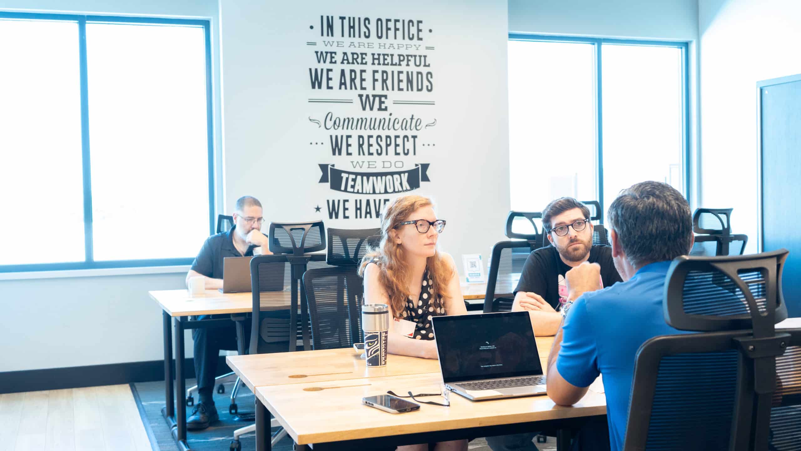 Teamwork in NuvoDesk Shared Desk Area ‣ NuvoDesk Coworking Members working near teamwork wall quote in NuvoDesk Coworking shared desk area