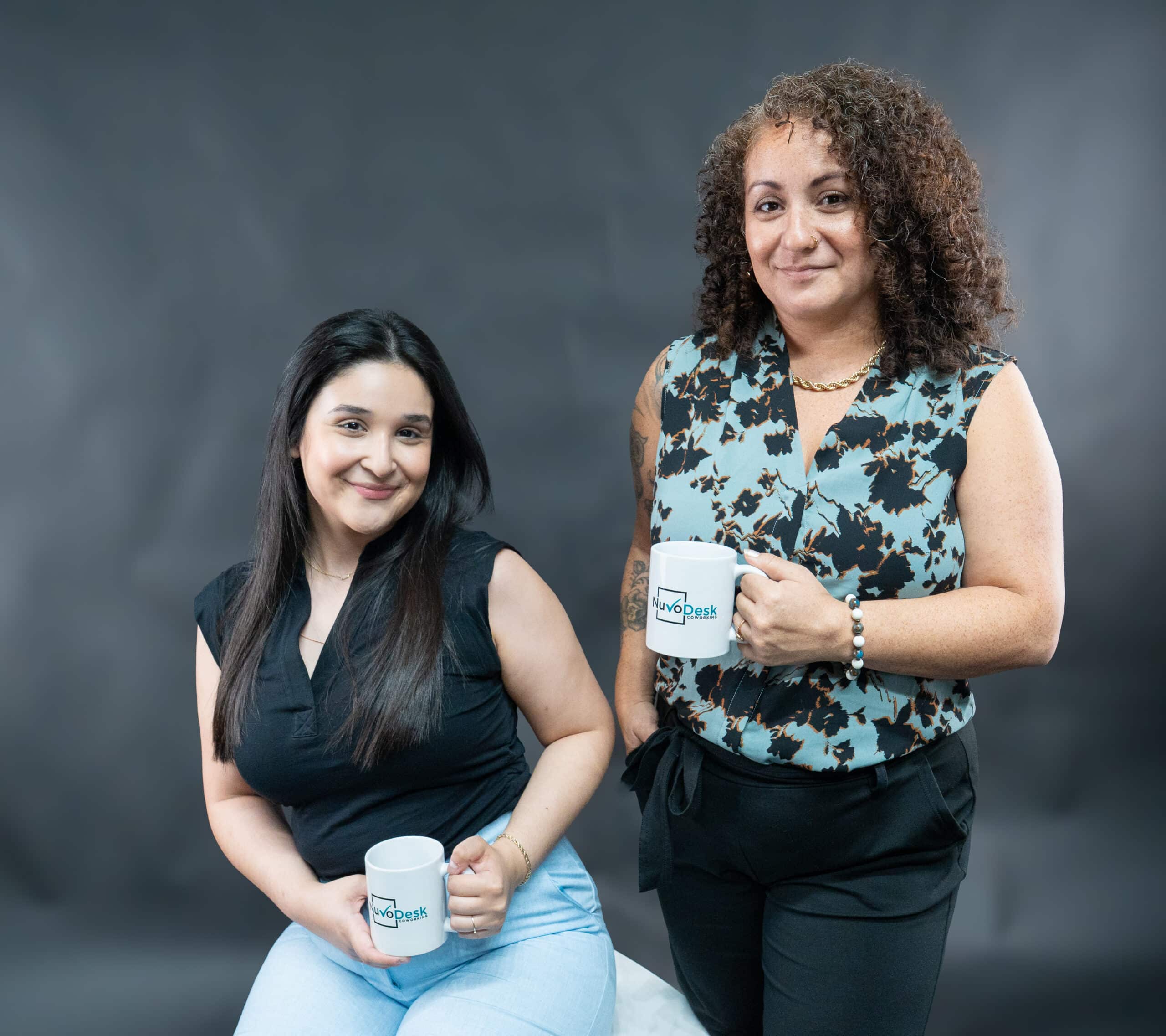 NuvoDesk Team Members Ivanna and Deanna ‣ NuvoDesk Coworking Ivanna sitting and Deanna standing with NuvoDesk mugs in team photo